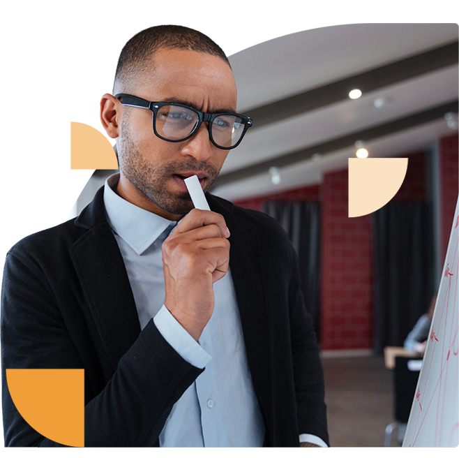 A serious cybersecurity professional with glasses and a suit thoughtfully holding a marker while looking at strategic plans on a whiteboard.