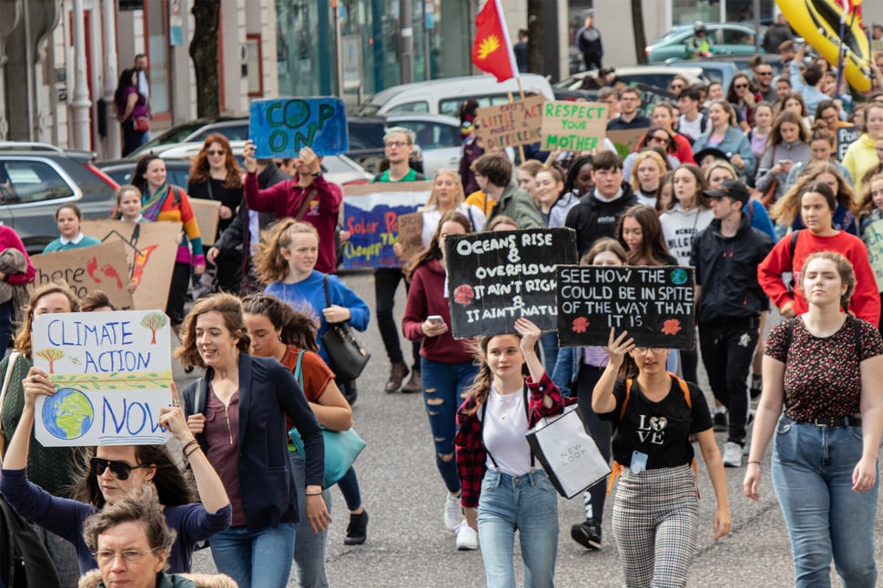 Menigte jonge activisten met protestborden over klimaatverandering, reflecterend hoe hacktivisme en fysieke protesten vaak dezelfde doelen nastreven.