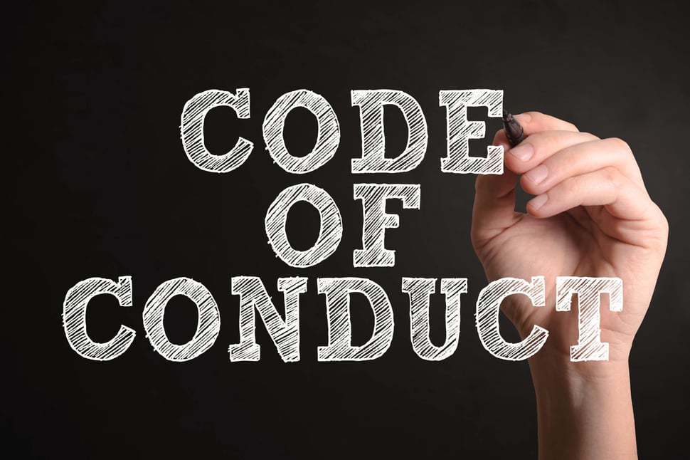 Een hand schrijft "Code of Conduct" op een zwarte achtergrond.