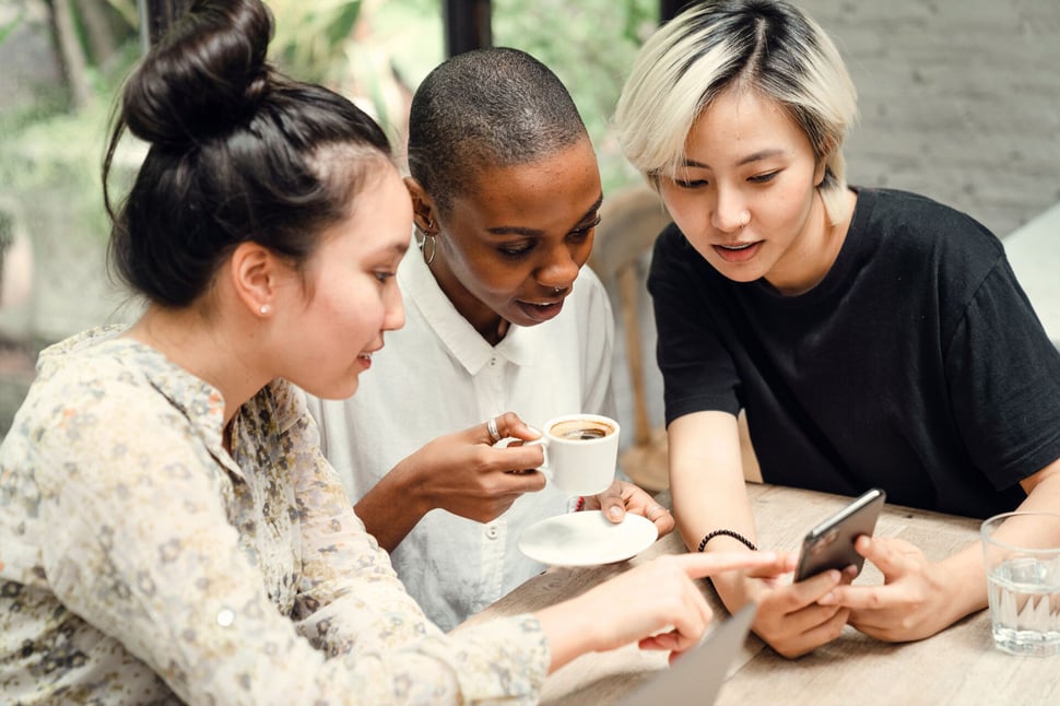 Groep collega's interacteert met een smartphone tijdens een koffiepauze, illustrerend hoe gemakkelijk de risico's van social media kunnen ontstaan.