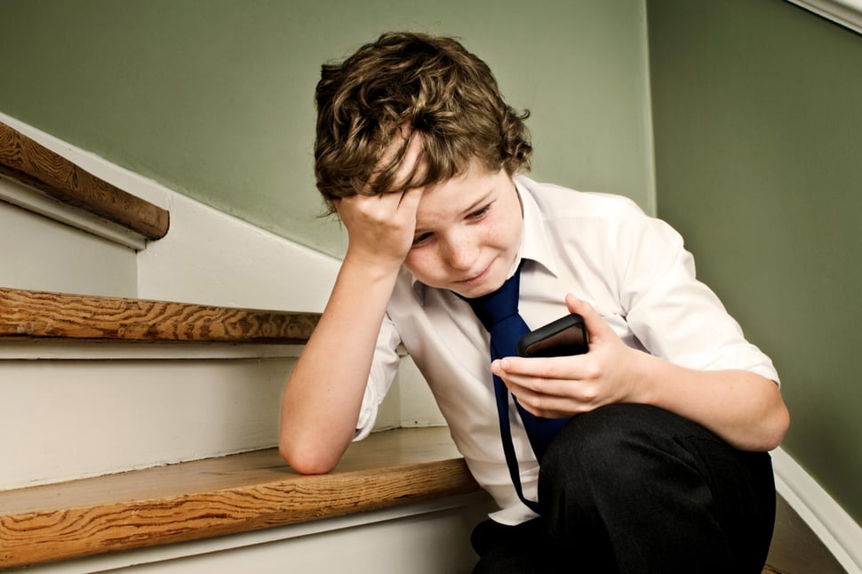 Verdrietige jongen op de trap kijkt naar zijn telefoon, mogelijk slachtoffer van cyberpesten.