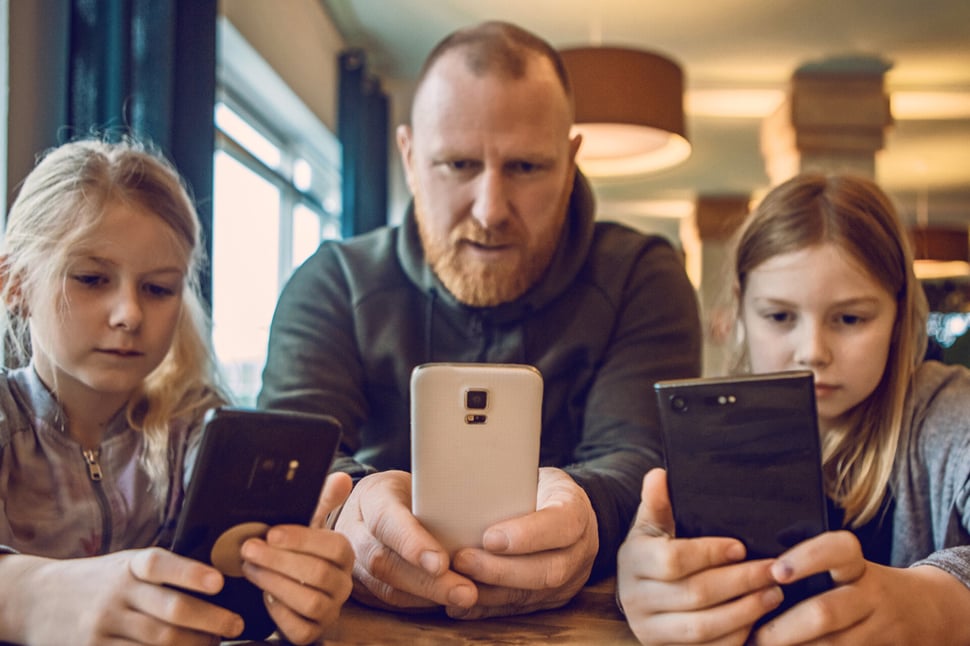 Vader en twee dochters kijken naar hun smartphones.