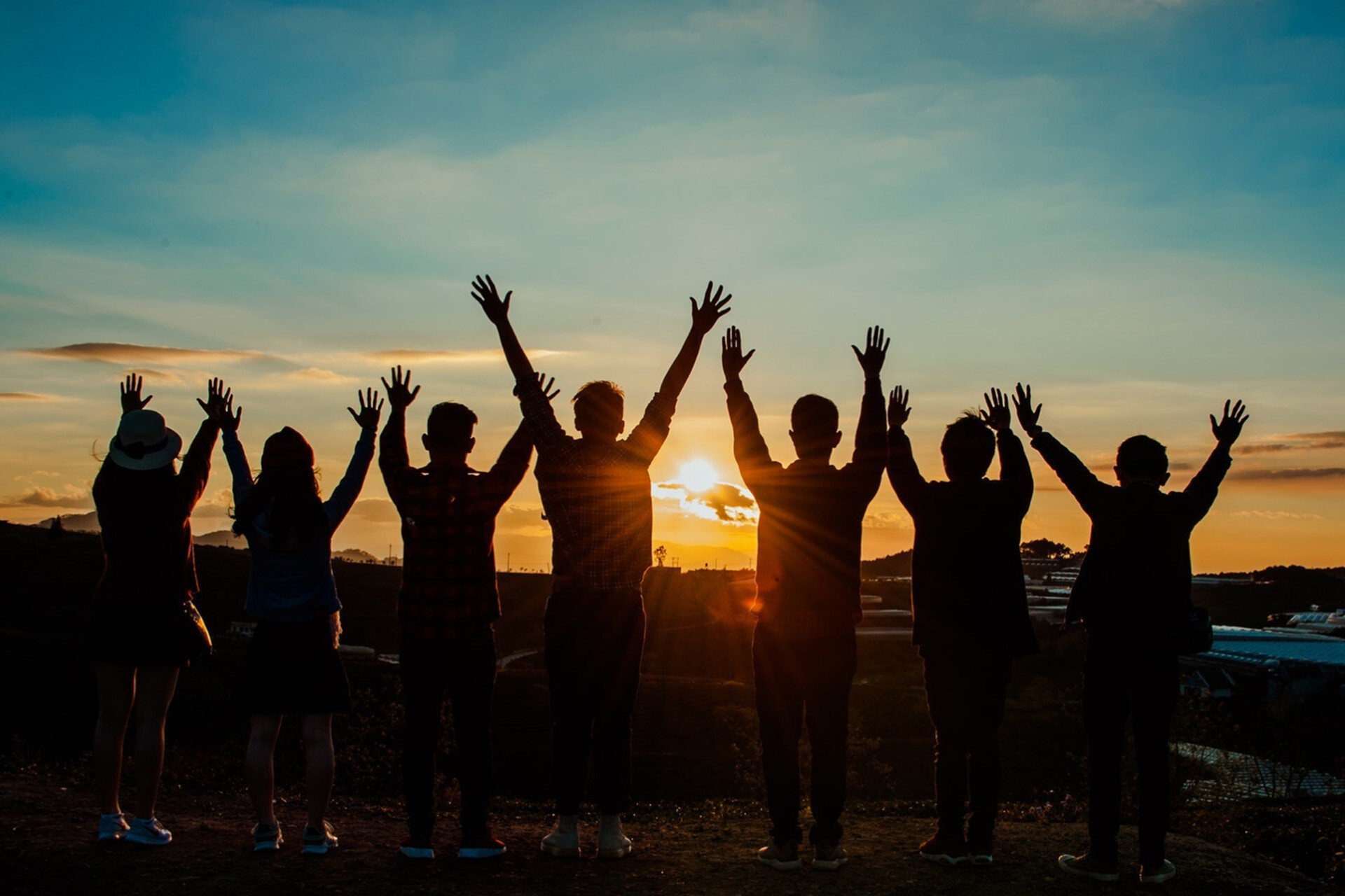 A sunrise in the background with a group of people cheering in the foreground. 