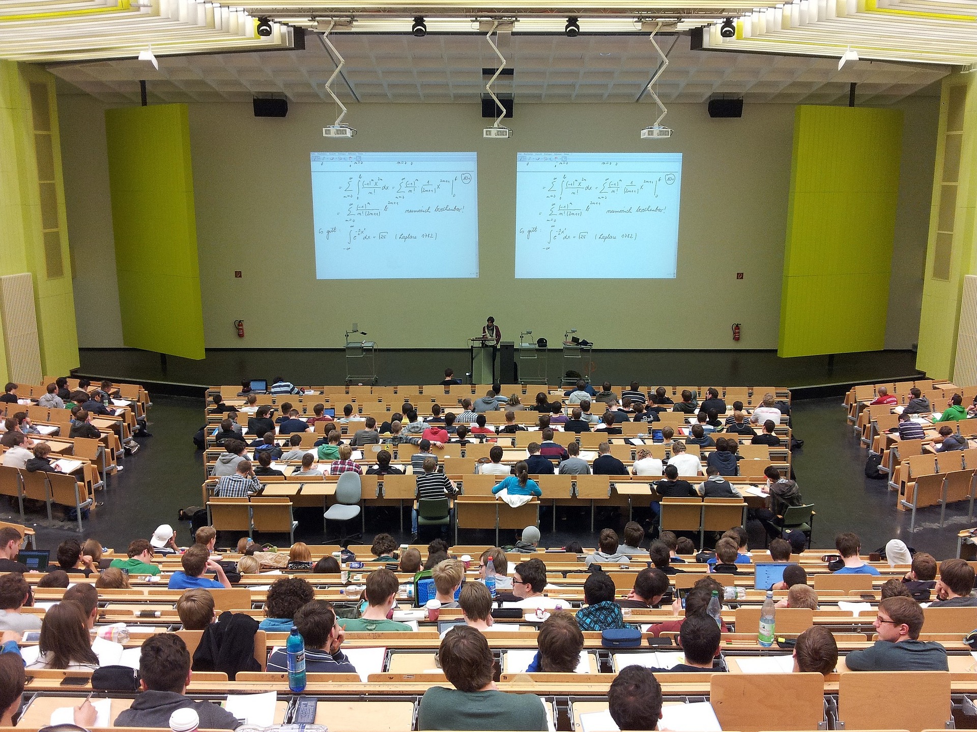 Foto van een congreszaal waarin veel studenten les krijgen van een docent.