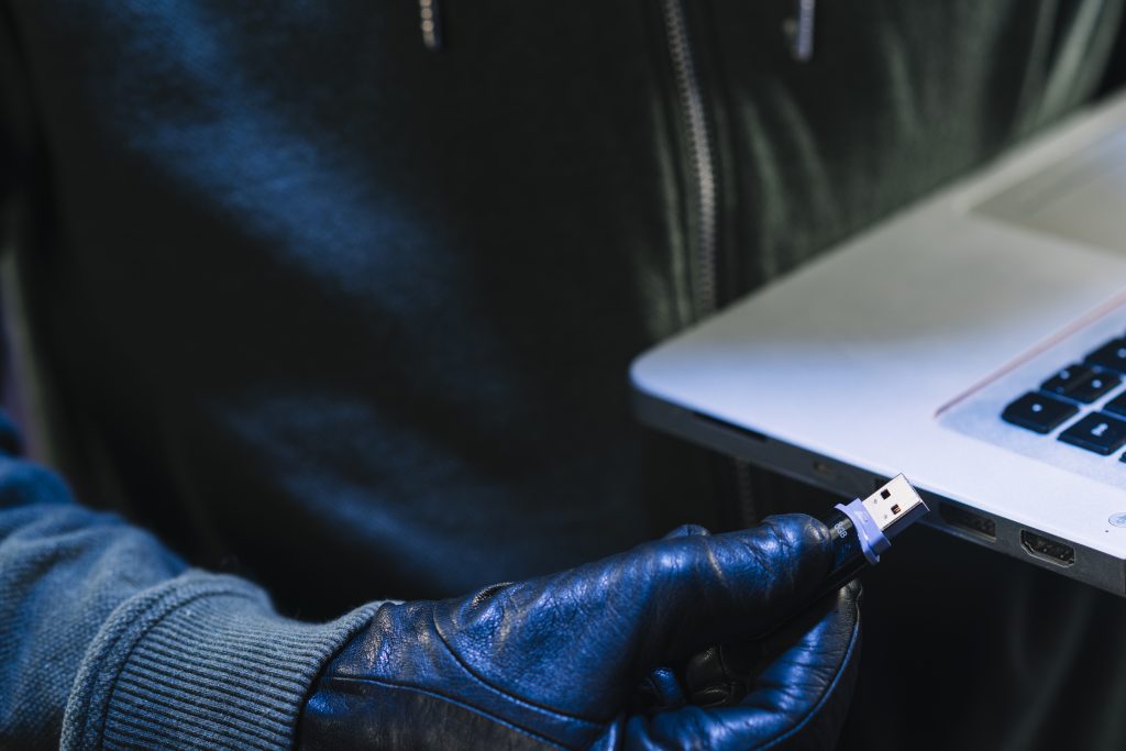 een foto van de hand van een hacker met een USB-stick die daarmee via een laptop een organisatie binnen wil dringen. 